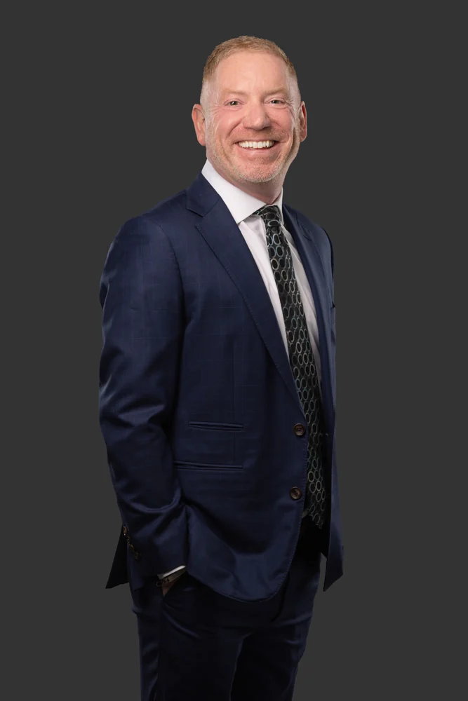 Jeffery R. Bray, standing portrait in a dark suit against a charcoal background.